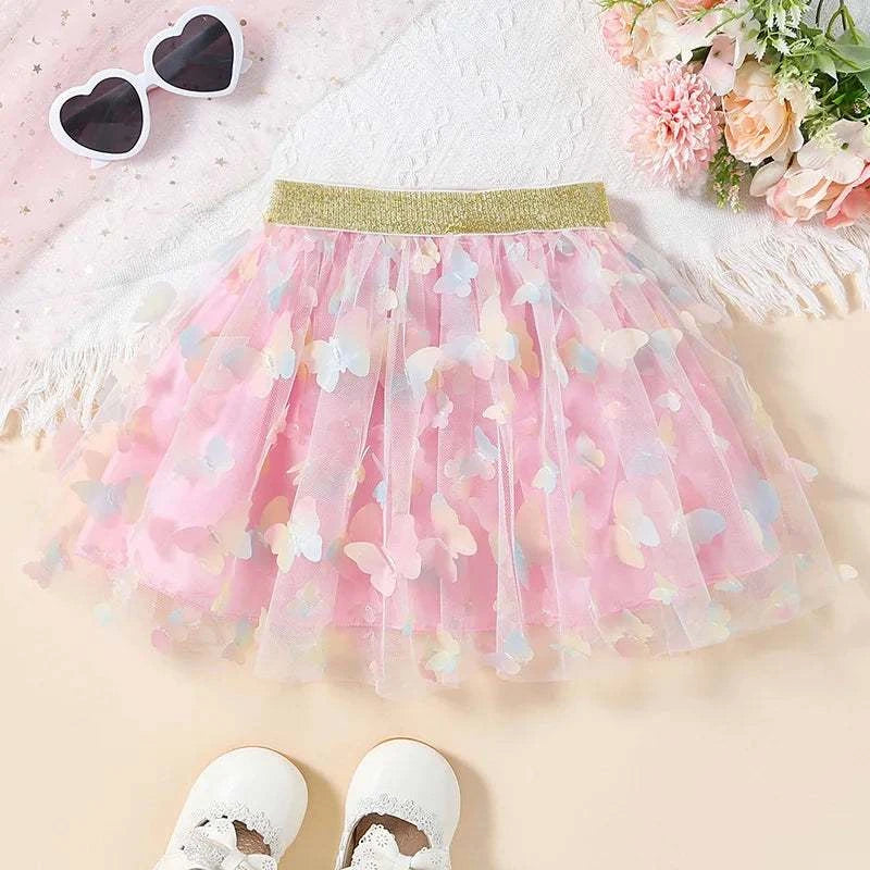 Pink baby girls tutu fluffy skirt with pastel butterfly prints and gold elastic waistband, laid flat with white heart-shaped sunglasses and white shoes nearby.