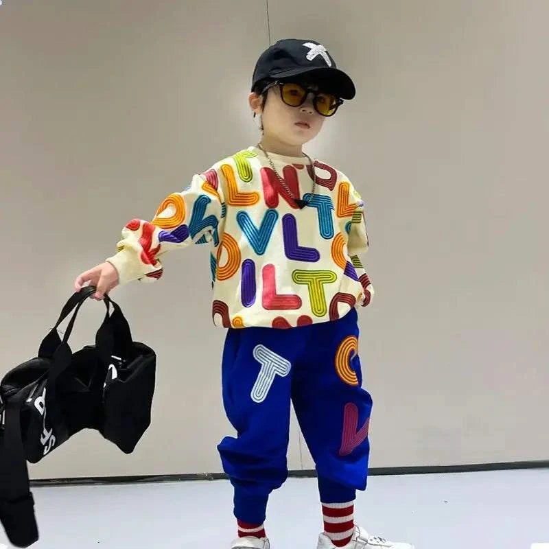 Boy wearing colorful letter print cotton pullover sweatshirt and blue sweatpants set with striped socks and black cap carrying black bag