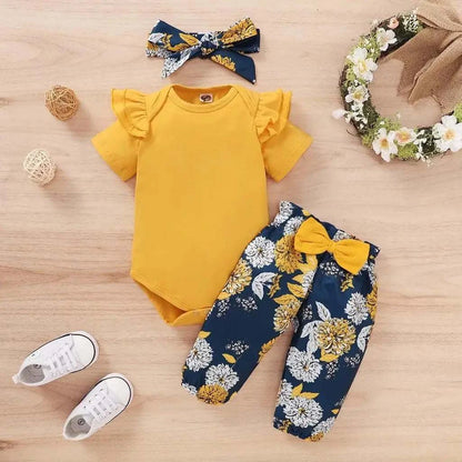Newborn baby girls' clothing set with yellow short sleeve bodysuit, floral navy pants with yellow bow, and matching headband.