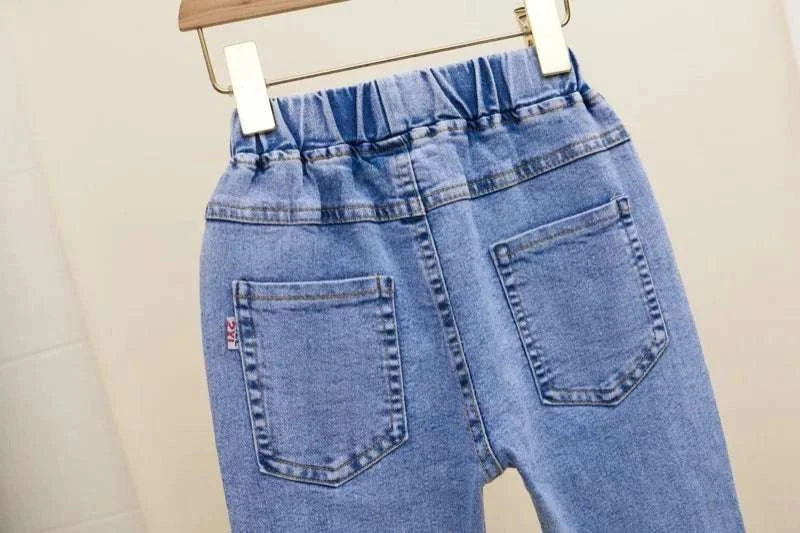 Back view of blue elastic waist casual girls' jeans with loose fit and two back pockets hanging on a wooden hanger